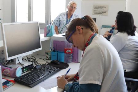 Professionals de l'Hospital Vall d'Hebron apuntant visites amb bolígraf i paper a la secretaria i la pantalla de l'ordinador apagada, davant la desconnexió generalitzada.